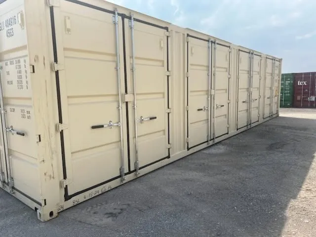 Beige open side shipping container with four sets of side doors on a gravel lot